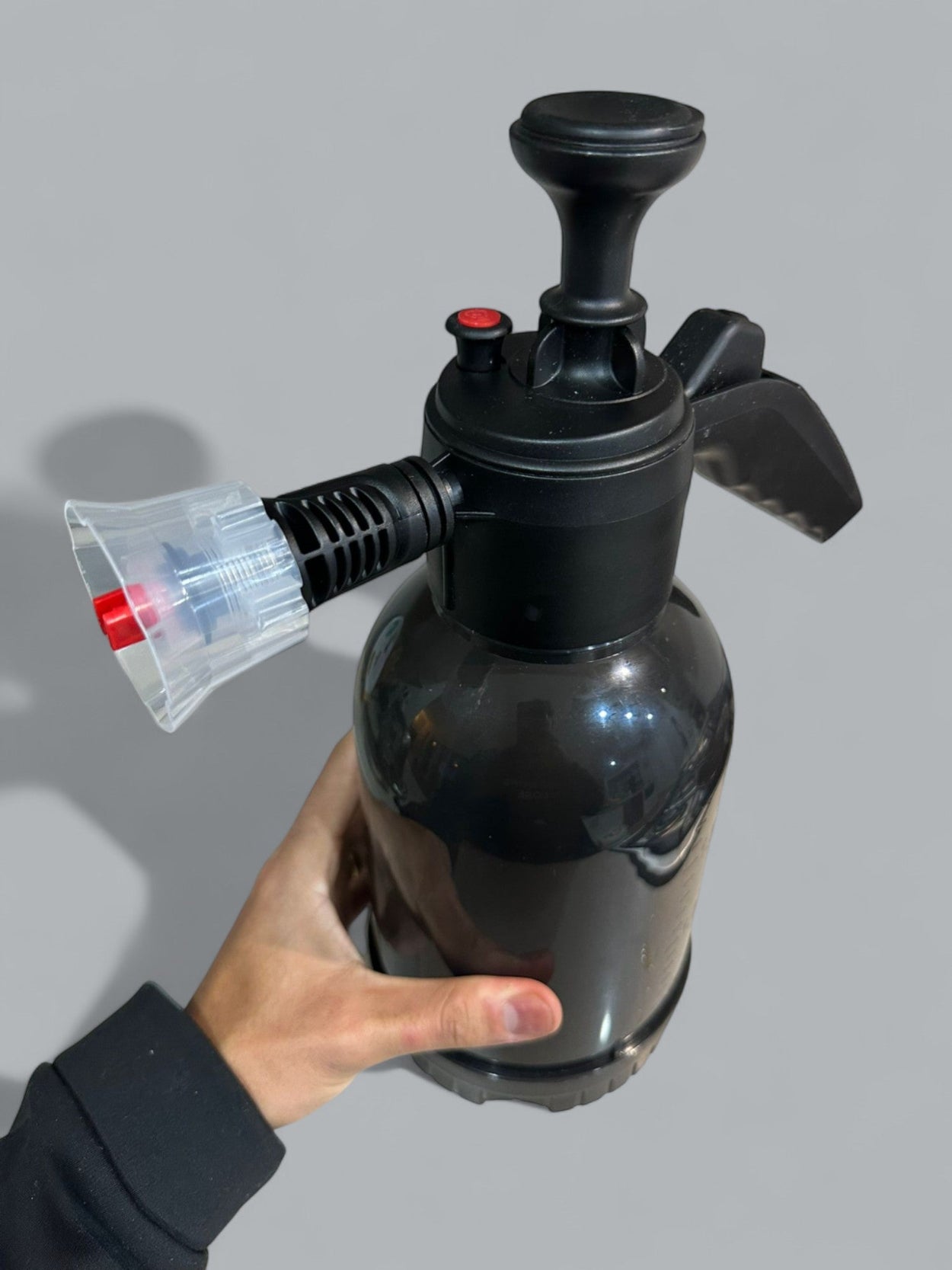Black spray bottle held by a hand against a gray background