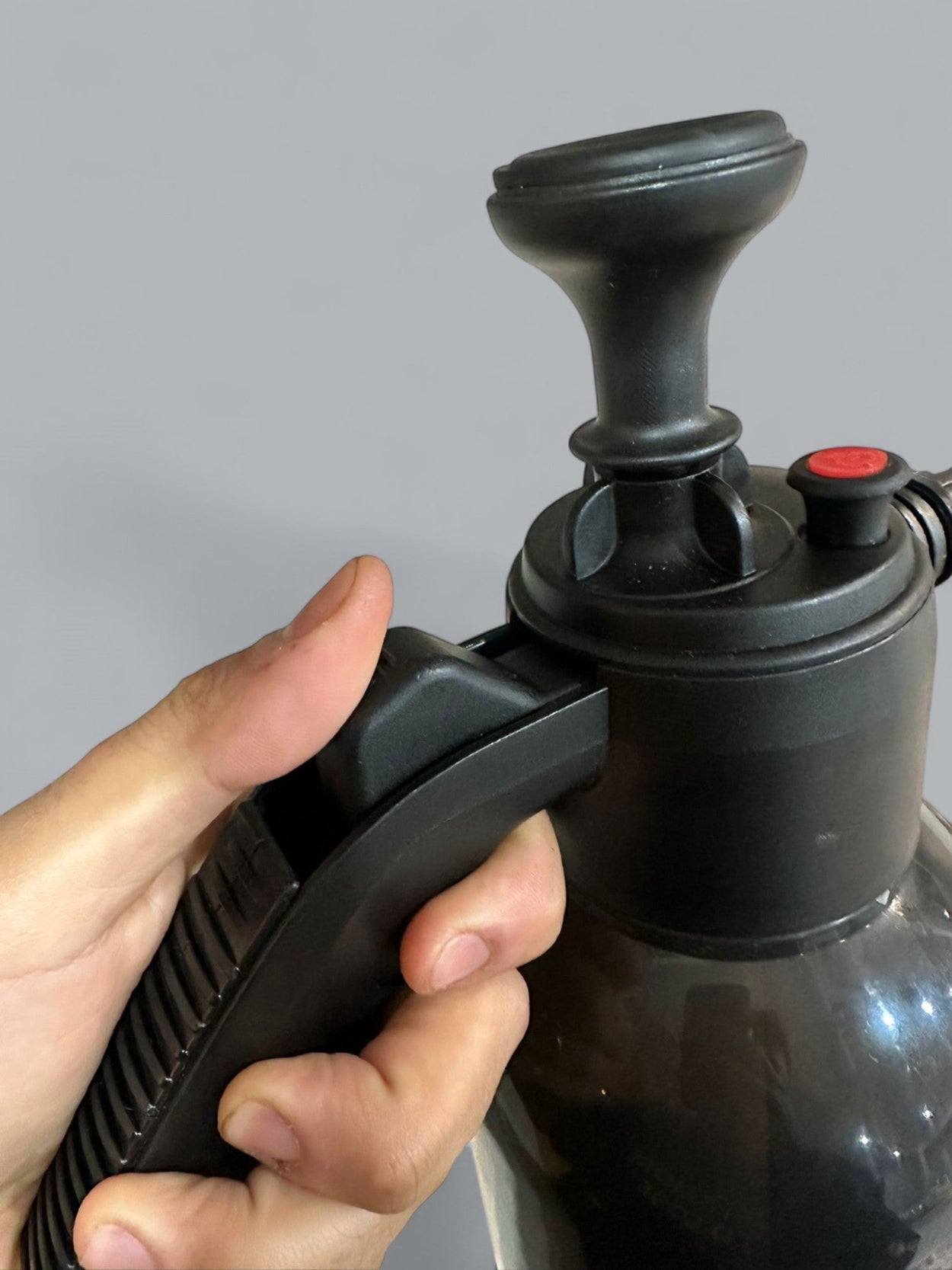 Hand holding a black pump with a red button against a gray background